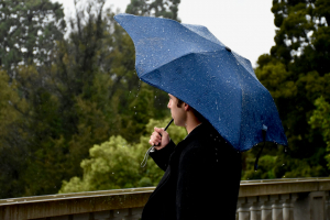 Mann mit blauem Regenschirm auf Brücke