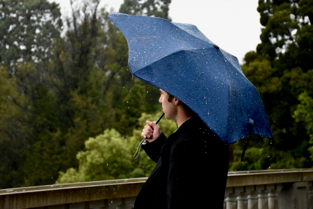 Mann mit blauem Regenschirm auf Brücke