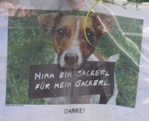 Ein Hund mit einem Schild: Nimm ein Sackerl für mein Gackerl.